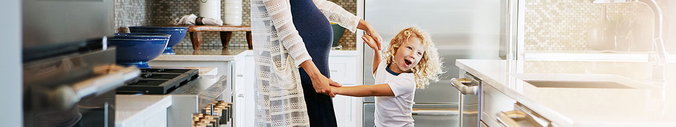 Pregnant mother and her daughter dancing in the kitchen.